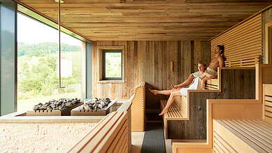 Entspanntes Paar in einer gemütlichen, mit Holz verkleideten Sauna im Familienhotel Schreinerhof im Bayrischen Wald.