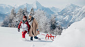 Winter im Salzburger Land: Familie macht eine Winterwanderung mit einem Schlitten. Bergpanorama im Hintergrund.
