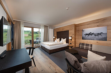 Geräumiges, modern eingerichtetes Hotelzimmer mit Holzakzenten und Pferdebild im Familienhotel Schreinerhof im Bayrischen Wald, mit Blick auf die grüne Landschaft.