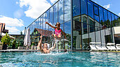 Familie planscht im großen Outdoor-Pool des Familienhotels Ulrichshof im Bayerischen Wald.