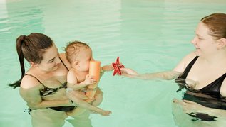 Eine Mutter ist im Hotel-Pool und hält ihr Baby im Arm.