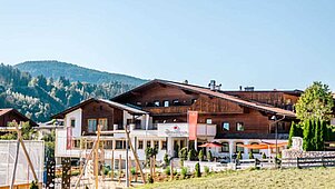 Das Familienhotel Das Hopfgarten in Tirol bei strahlenden Sonnenschein von außen. Auf dem Hotelgelände befindet sich ein großzügiger Outdoor-Spielplatz.
