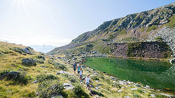Familie wandert rund um einen tiefgrünen Bergsee in Südtirol.