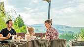 Familie sitzt auf der Terrasse des Familienhotels Schreinerhof und genießt ihr Frühstück in der Sonne.