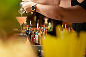 Ein Barkeeper gießt einen orangefarbenen Cocktail in ein Martiniglas an einer voll ausgestatteten Hotelbar im Familienhotel Schreinerhof