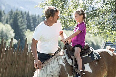 Vater sieht seinem Kind beim Ponyreiten im Familienurlaub im Mons Silva Private Luxury Chalets in Südtirol zu.