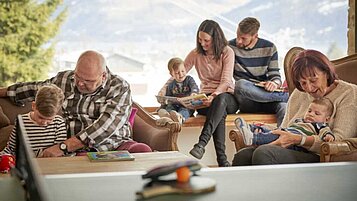 Großfamilie sitzt im gemütlichen Loungebereich des Familienhotels Amiamo im Salzburger Land. Die Kinder spielen mit altersgerechten Spielsachen.