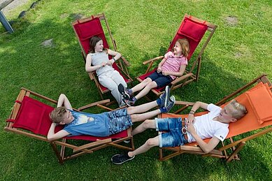 Jugendliche Kinder liegen im Liegestuhl im Garten und Verweilen gemeinsam im Familienhotel Landhuus Laurenz.