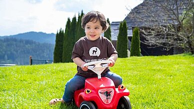 Ein kleiner Junge sitzt auf einem roten Bobbycar im Familienhotel Petschnighof in Kärnten