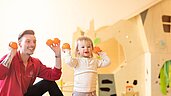 Kinderbetreuer und Kleinkind spielen gemeinsam mit Bällen im Happy-Club des Familienhotels Sonnenpark.