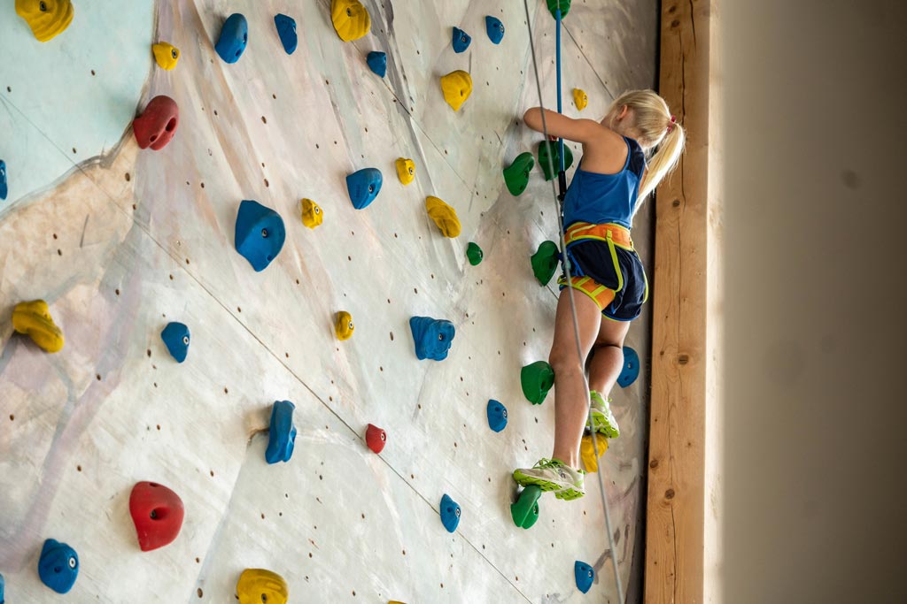 Ein Kind klettert die Klettwand im Almfamilyhotel Scherer hinauf 