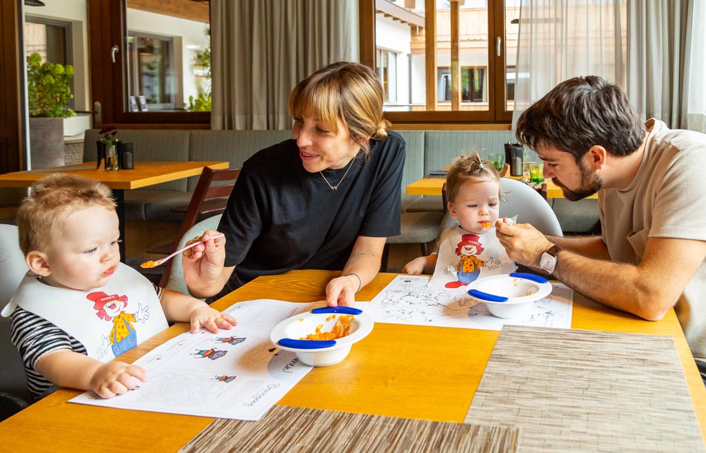 Eine Familie sitzt am Essenstisch und die Eltern füttern die beiden Babys im Familienhotel Das Bayrischzell in Oberbayern