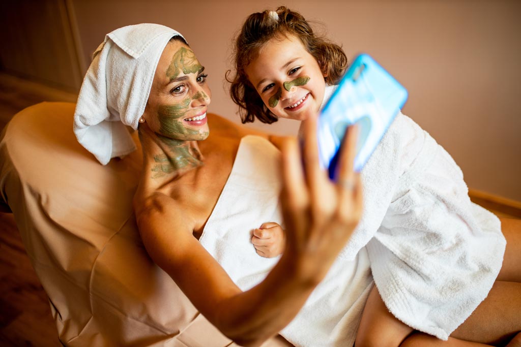 Eine Mutter mit ihrem Kind bei einer Gesichtsbehandlung und machen ein Selfie mit dem Handy im Familienhotel Das Bayrischzell in Oberbayern