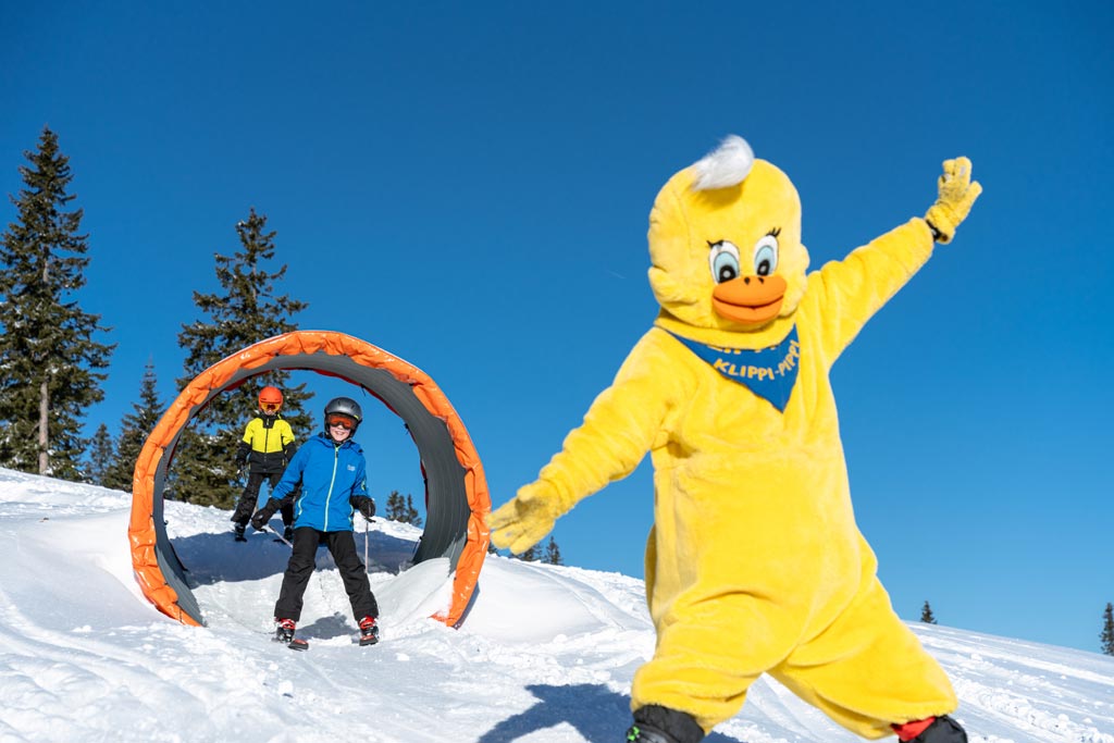 Kinder fahren auf Skiern durch einen Tunnel im Winter-Familienurlaub in Kärnten 