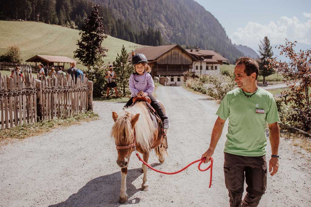 Mädchen sitzt auf einem Pony und wird von einem Kinderbetreuer geführt.