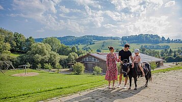 Mädchen sitzt auf einem Pony. Die Eltern stehen daneben und halten die Leine des Ponys in der Hand.