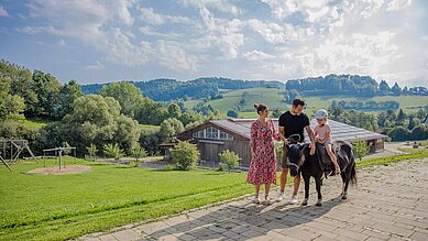 Mädchen sitzt auf einem Pony. Die Eltern stehen daneben und halten die Leine des Ponys in der Hand.