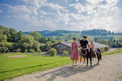 Mädchen sitzt auf einem Pony. Die Eltern stehen daneben und halten die Leine des Ponys in der Hand.