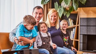 Familie mit drei Kindern sitzt zusammen auf einer gemütlichen Couch in der Lobby des Familienhotels Aigo im Böhmerwald.