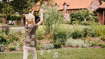 Ein Junge spielt mit Seifenblasen im Garten im Aussenbereich im Landhaus Averbeck in der Lüneburger Heide. 