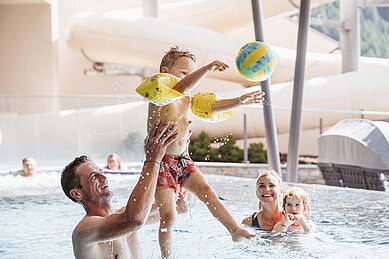 Familie planscht fröhlich im hellen Hallenbad des Familienhotels Huber in Südtirol