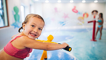 Mädchen spielt auf dem Wasserspielplatz im Hallenbad des Familienhotels Kirchheimerhof in Kärnten mit einer Wasserpistole.