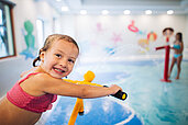 Mädchen spielt auf dem Wasserspielplatz im Hallenbad des Familienhotels Kirchheimerhof in Kärnten mit einer Wasserpistole.