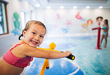 Mädchen spielt auf dem Wasserspielplatz im Hallenbad des Familienhotels Kirchheimerhof in Kärnten mit einer Wasserpistole.