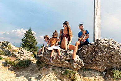 Familie pausiert am Gipfelkreuz von der schönen Familienwanderung in Vorarlberg.