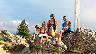 Familie pausiert am Gipfelkreuz von der schönen Familienwanderung in Vorarlberg.