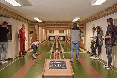 Eine Familie spielt Kegeln auf der hauseigenen Kegelbahn im Familienhotel Zauchenseehof im Salzburger Land.