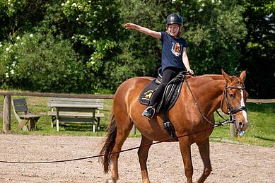 Mädchen sitzt fröhlich auf einem Pferd auf dem Reitplatz des Bernsteinreiter Schlossresorts