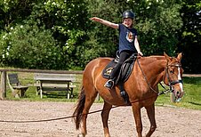 Mädchen sitzt fröhlich auf einem Pferd auf dem Reitplatz des Bernsteinreiter Schlossresorts