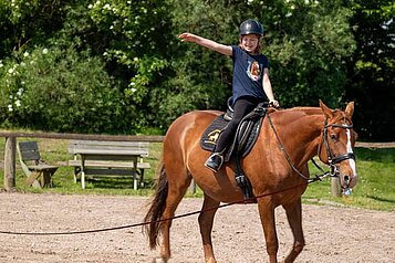 Mädchen sitzt fröhlich auf einem Pferd auf dem Reitplatz des Bernsteinreiter Schlossresorts