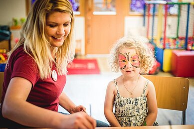 Ein Kind mit einer Kinderbetreuerin beim Kinderschminken im Landgut Furtherwirt in Tirol ab.