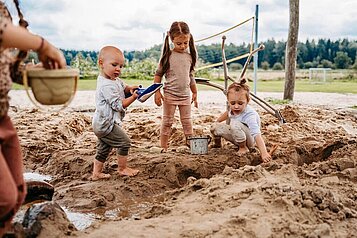 Kinder spielen mit Spielsachen im Sandkasten auf dem Außengelände des Familienhotels Landhaus Averbeck in der Lüneburger Heide.