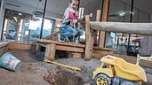 Ein Kind spielt mit einer Gießkanne im Indoor-Matschplatz im Almfamilyhotel Scherer in Tirol.