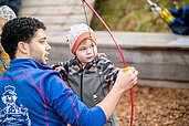 Betreuer ist mit seinem Schützling draußen Bogenschießen auf dem Outdoor-Gelände des Familienhotels Landhaus zur Ohe im Bayerischen Wald.