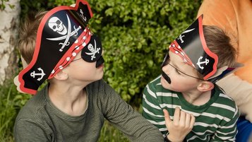 Zwei verkleidete Piratenkinder mit Hüten und Augenklappen genießen ein fantasievolles Abenteuer im Freien.