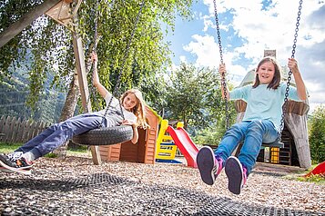 Kinder schaukeln auf dem Spielplatz im Familienhotel Kinderhotel Sailer in Pitztal.