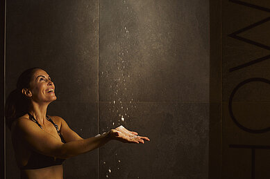 Frau nimmt in der Wellness Dusche eine Abkühlung im Familienhotel Alpenhotel Kindl in Tirol.