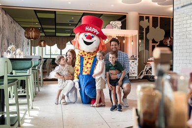 Die Familie macht ein Erinnerungsfoto mit dem Maskottchen Happy in der Lobby des Familienhotels.