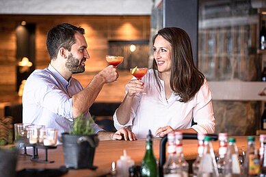 Eltern sitzen gemeinsam an der Bar und trinken einen Cocktail im Allgäuer Berghof.