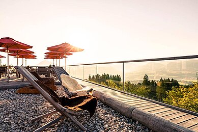 Sonnenterrasse mit Liegestühlen und roten Sonnenschirmen und Blick in die Berge im Familienhotel Allgäuer Berghof.