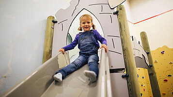 Mädchen rutscht eine Ritter-Rutsche im Happy-Club des Familienhotels Kirchheimerhof in Kärnten hinunter.