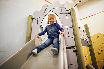 Mädchen rutscht eine Ritter-Rutsche im Happy-Club des Familienhotels Kirchheimerhof in Kärnten hinunter.