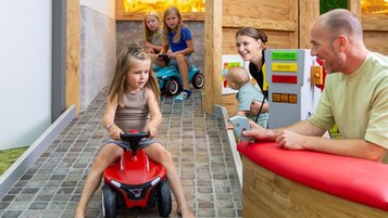 Familie spielt im Indoor-Spielbereich des Familienhotels Rhön Feeling, die Kinder fahren auf dem Bobby Car