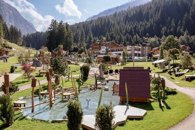 Außenansicht des Familienhotel Habachklause im Sommer mit großem Abenteuerspielplatz und umliegender Bergkulisse.