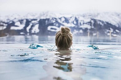 Frau schwimmt im Outdoor Pool des Allgäuer Berghofs mit Blick in die beschneiten Berge.