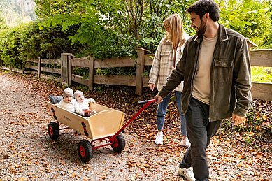 Zwei kleine Kinder sitzen in einem Bollerwagen und werden vom Vater gezogen - Familienhotel Das Bayrischzell in Oberbayern